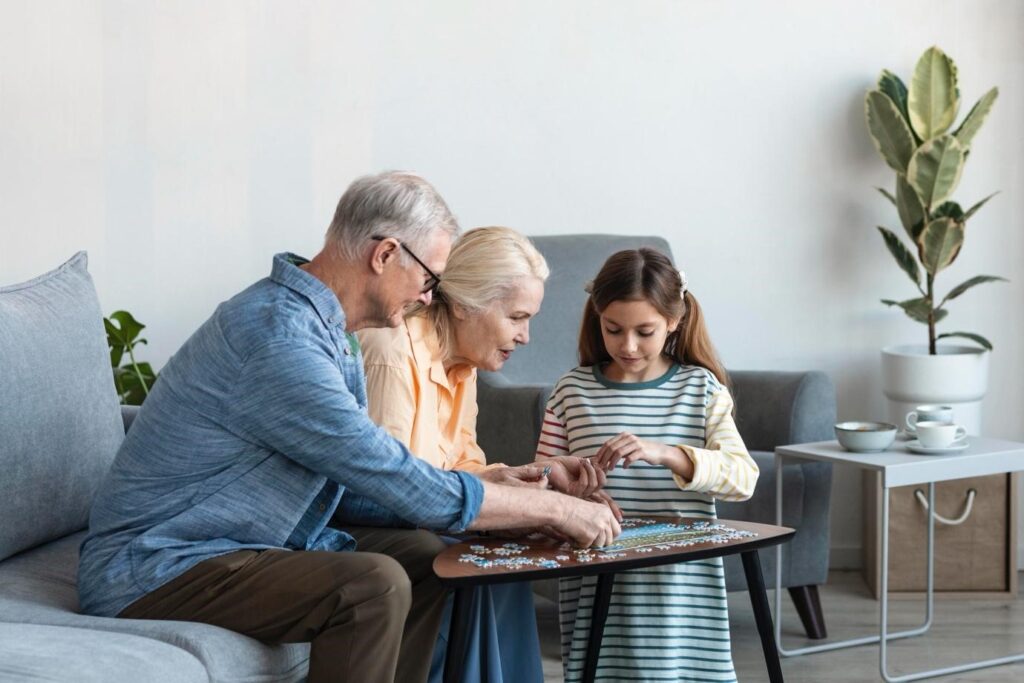 Senior couple and young girl solving a puzzle together at a small table in a cozy living room, enjoying quality family time.