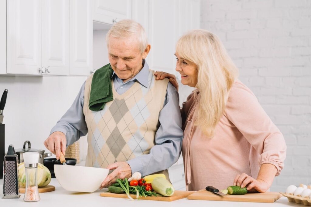 Smiling senior couple cooking together in a bright kitchen, preparing fresh vegetables and sharing a warm moment.