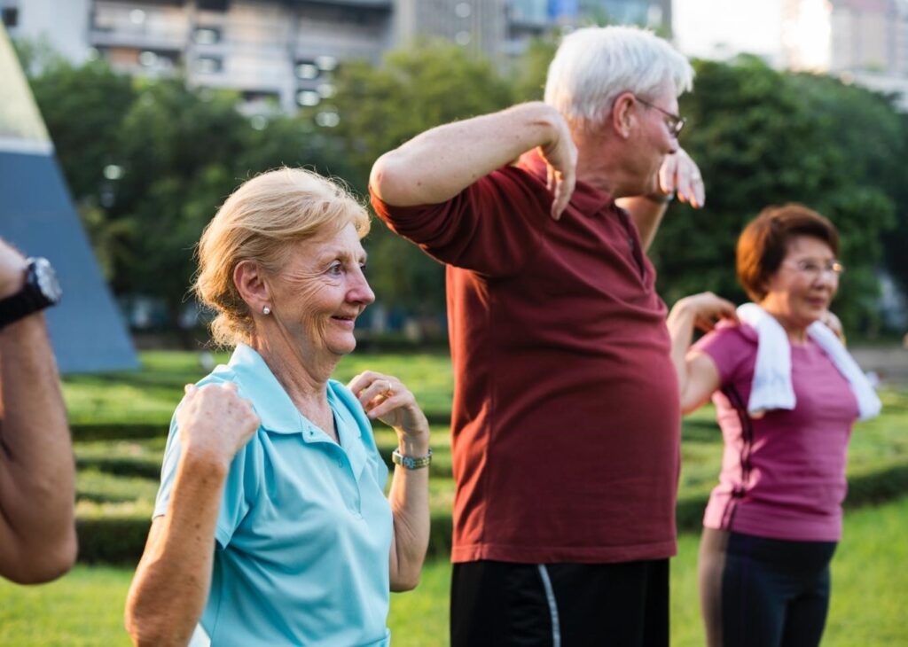 Group of active seniors exercising together in a park, smiling and stretching as part of a healthy lifestyle routine.
