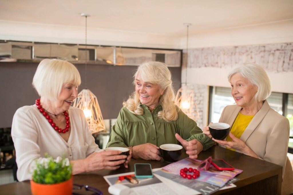 Three elderly women sitting at a café table, drinking coffee and enjoying a cheerful conversation.