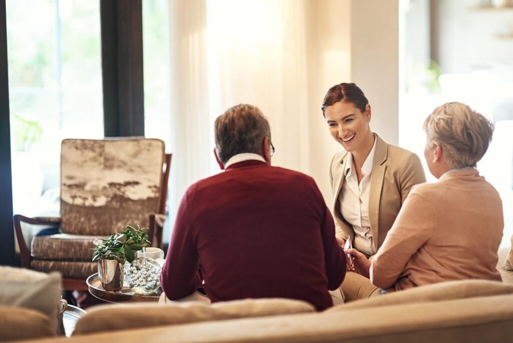 A smiling consultant talking with an elderly couple in a cozy living room during a retirement planning discussion.