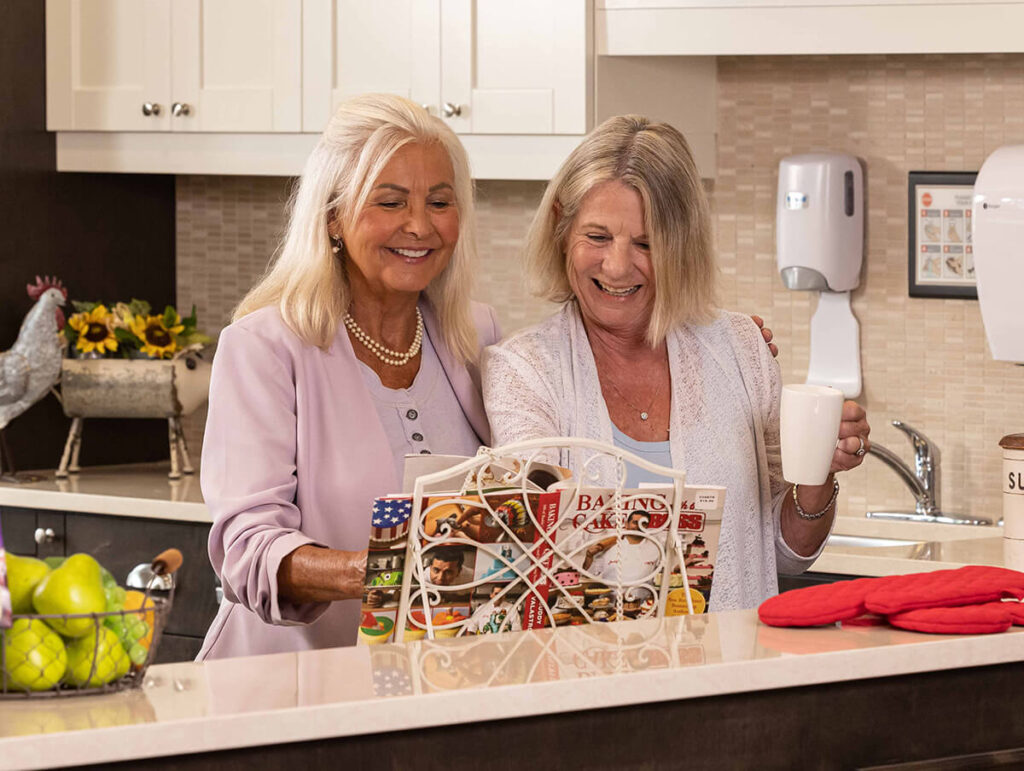 Two senior females chatting over coffee in kitchen.