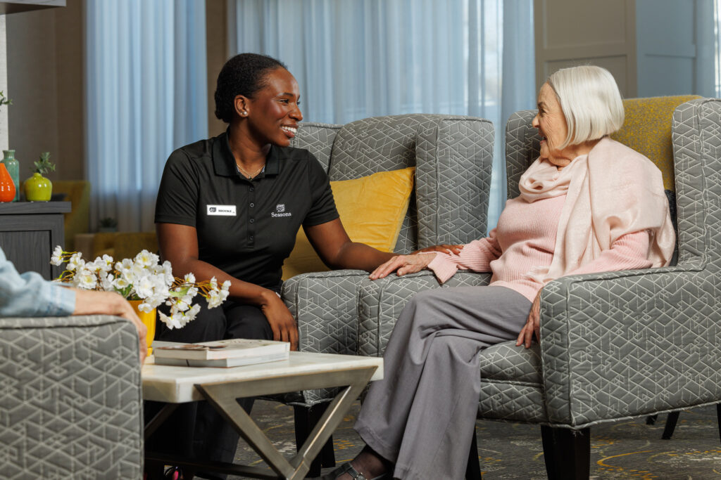 Seasons Retirement team member sitting and speaking with female residents in lounge.