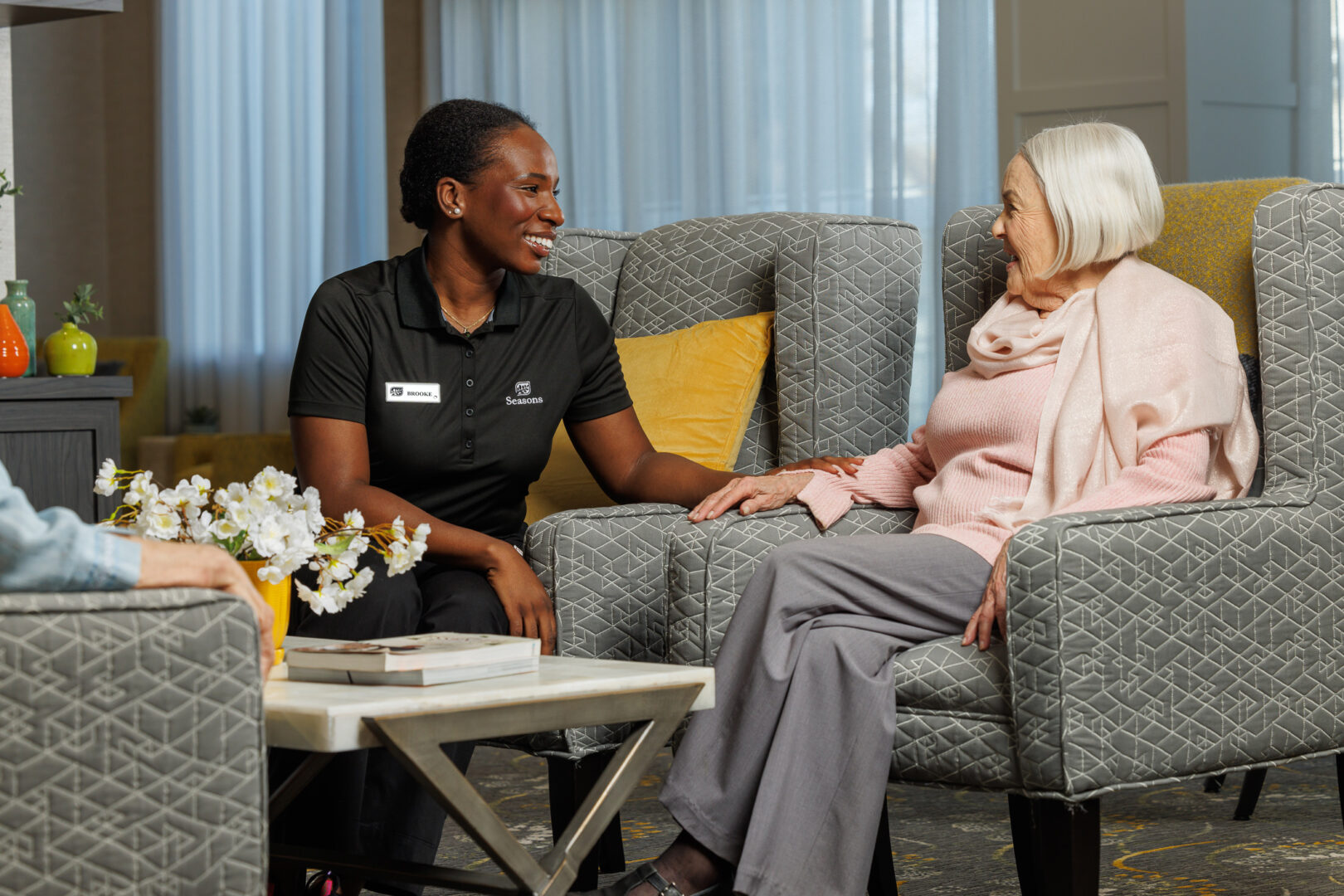 Seasons Retirement team member sitting and speaking with female residents in lounge.