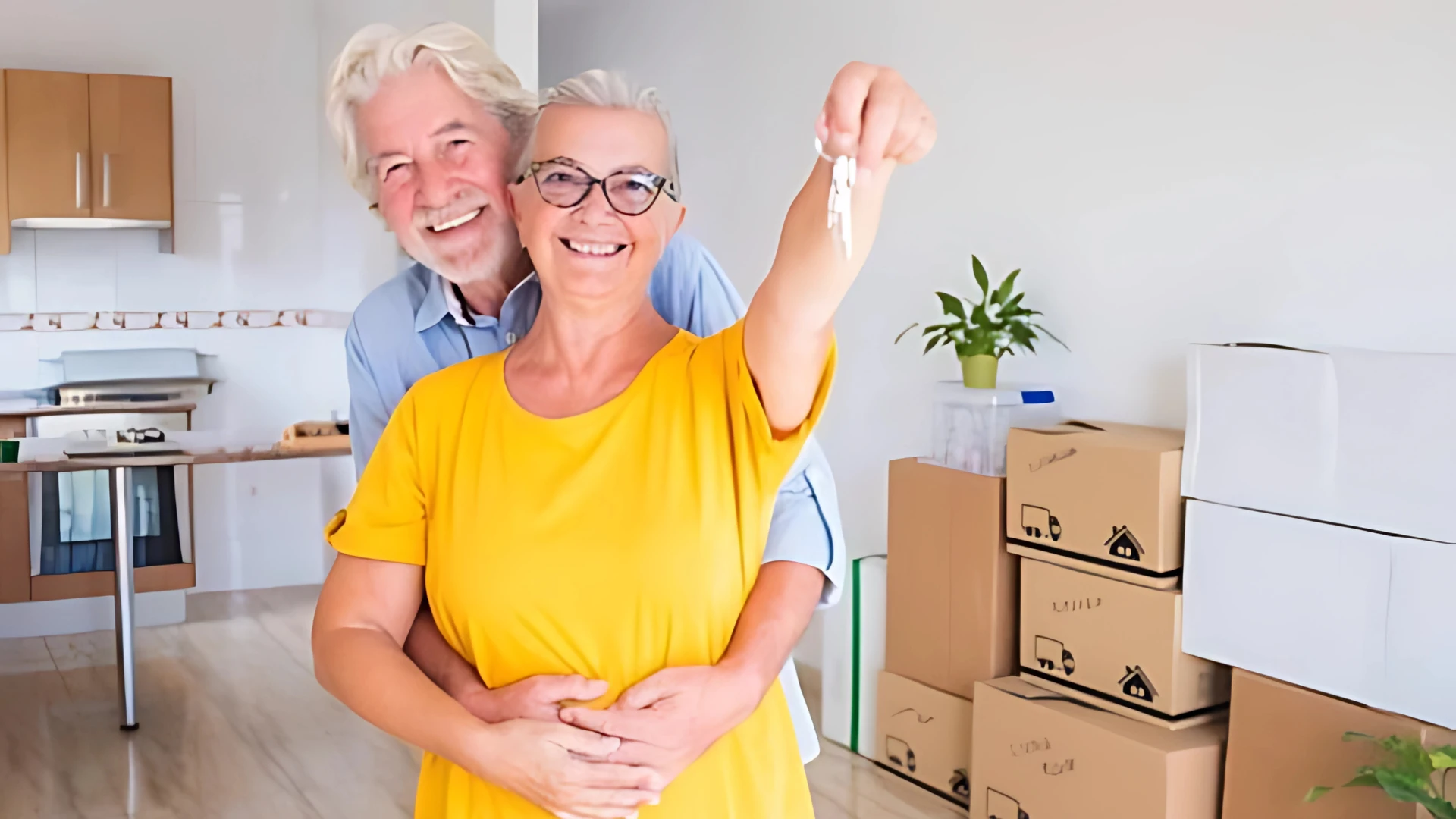 Happy senior couple holding keys in their new home, surrounded by moving boxes during their transition to a retirement community.